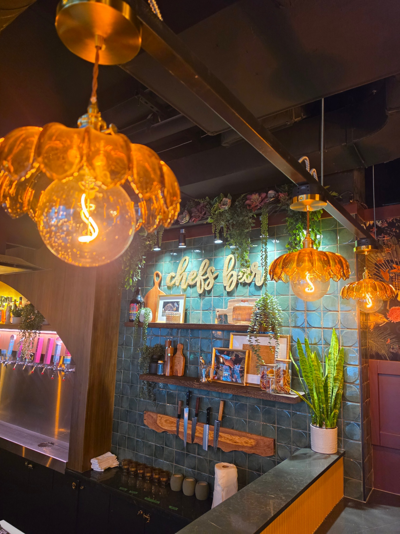 Chef's bar with teal tile, hanging amber pendants, and knife display